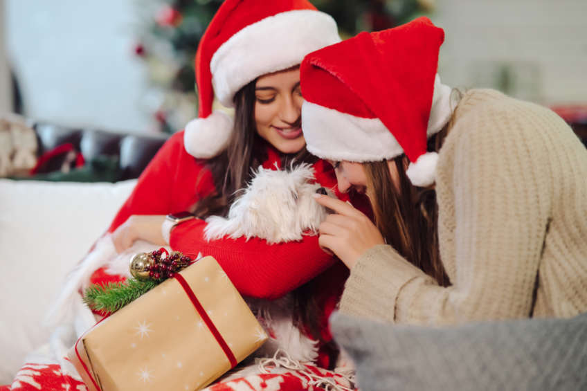 Dos chicas acarician a un cachorrito blanco como regalo de Navidad